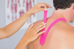 Physiotherapist putting on pink kinesio tape on male patients neck in bright office